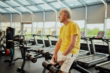 Mature, sportive man resting standing near training equipment during exercise session at modern...