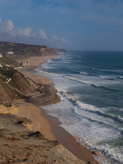 AERIAL: Coastal cliffs rising above sandy shoreline with lapping ocean waves. Rugged beauty of...