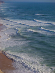 Rolling blue ocean waves washing ashore on a beautiful sandy beach in Portugal. Mesmerizing view of...