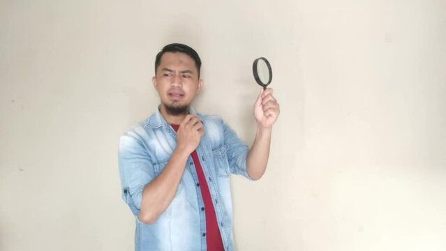 Asian man is looking at something using a magnifying glass with a confused expression