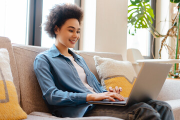 Happy, beautiful African American woman, freelancer using laptop, watching video, checking email