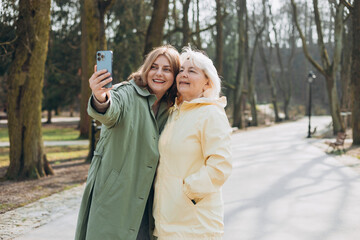 Happy older Mother and adult daughter are doing Selfie on city street. Outdoor shot of well-dressed female friends. Two women together doing selfie shot on mobile cell phone. Family day concept.