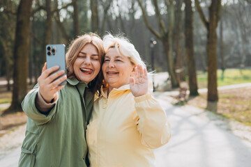 Happy older Mother and adult daughter are doing Selfie on city street. Outdoor shot of well-dressed female friends. Two women together doing selfie shot on mobile cell phone. Family day concept.