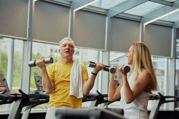 Fototapeta na wymiar Mature couple, man and woman in sportswear doing exercises for hands with dumbbells in modern gym. Concept of sport, active seniors in modern life, healthy lifestyle, fitness centers for retirements.