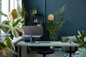 Background image of modern office workplace with computer and green plants against blue wall copy...