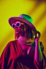 Urban style meets playful elegance. Female model posing in hat, retro style sunglasses and dress...