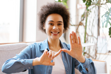 Attractive young African American woman with curly hair gesturing, communicating with sign language