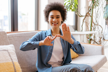 Smiling African American curly haired woman wearing casual clothes communicating with sign language