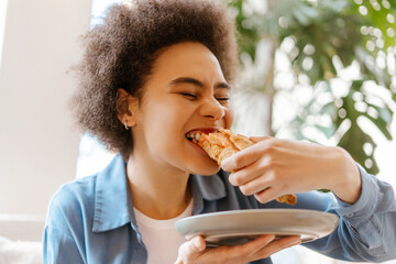 Closeup portrait of beautiful, attractive young African American woman eating tasty, fresh croissant