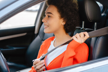 Beautiful, smiling, young African American woman, driver with curly hair fastens seat belt