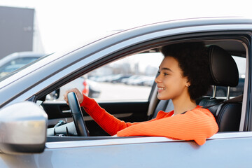 Beautiful attractive young African American woman with curly hair driving car, buckled safety belt