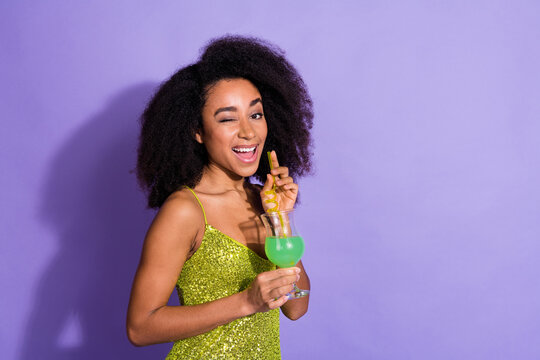 Photo portrait of gorgeous young girl hold cocktail wink wear trendy green sequins outfit isolated on purple color background