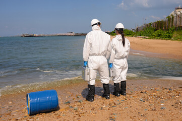 Ecologists in protective suits working near the coastline and taking samples of water for analysis