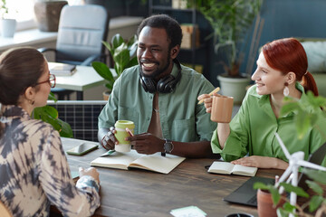 Multiethnic team of smiling young business people collaborating in office sitting at meeting table in green office