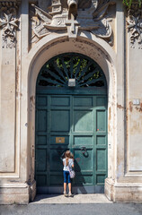 Fototapeta na wymiar Little girl on tiptoe looking at St. Peter's dome from the hole of the door of Villa del Priorato of Malta on Aventino Hill at Knights of Malta square, Rome, Italy