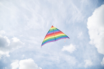Colorful rainbow Kite flying high in the blue gray sky. Isolated kite on the blue background. Weekend leisure entertainment activities. Peaceful relaxation. Time with loved one, children and family.