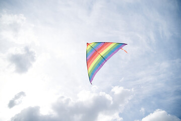 Colorful rainbow Kite flying high in the blue gray sky. Isolated kite on the blue background. Weekend leisure entertainment activities. Peaceful relaxation. Time with loved one, children and family.