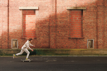 Side view of energetic young man with curly hair in casual clothes skating and having fun in city.