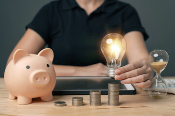 Hand holding a light bulb on a pile of money. Ideas for saving energy to save expenses. Money saved...