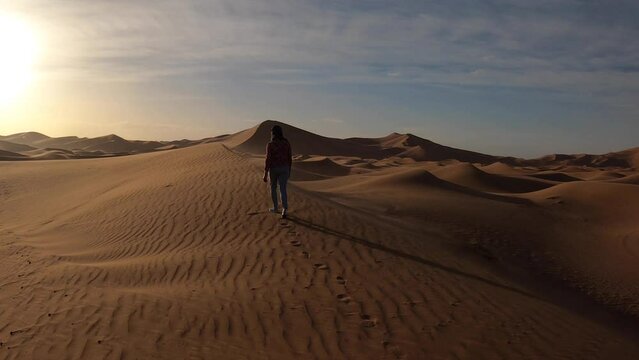 Lonely woman walking through sand dunes of Erg Chebbi in the Sahara desert at sunrise, Morocco
