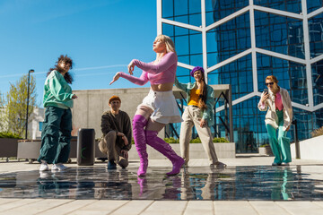 Outdoor Scene Of Young Adults Dancing Joyfully In An Urban Setting, With A Modern Glass Building In The Background, Reflecting Youth Culture And Friendship Through Dynamic Movement And Colorful Attire