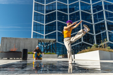 Vibrant Outdoor Scene Captures A Young Woman In A Yellow Top And Purple Hat Dancing Energetically, With A Male Spectator In Yellow Pants And A Blue Hat, Against A Modern Glass Building Background.