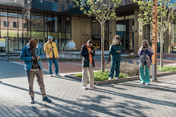 Young Adults Using Smartphones On A City Street, Engaged In Social Media, Posting Content, Dressed...