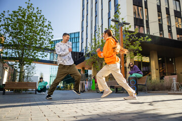 Vibrant Outdoor Scene Of Young Adults Joyfully Dancing On A Sunny Day In An Urban Setting,...