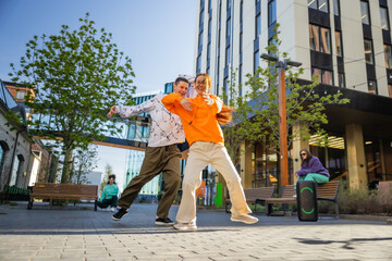 Vibrant Outdoor Scene Capturing Two Young Adults Joyfully Dancing In An Urban Setting, Showcasing...