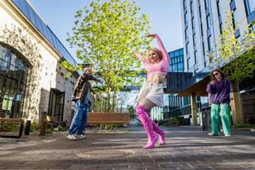 Vibrant Outdoor Scene Of Young Adults Dancing In An Urban Setting, With A Woman In Pink Leading...