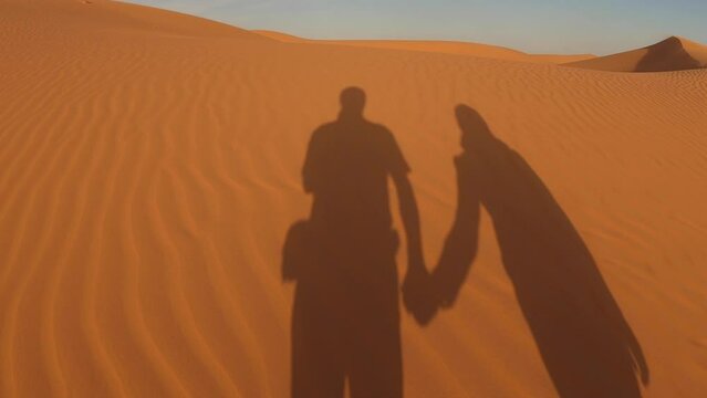Silhouette of loving couple walks holding hands along the sandy dunes of Erg Chebbi, Morocco