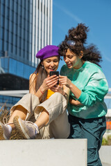Two Young Women Sharing A Laugh While Looking At A Smartphone In A City Setting, Showcasing Friendship And Technology. Vertical Screen, Perfect For Modern Lifestyle And Connectivity Themes.