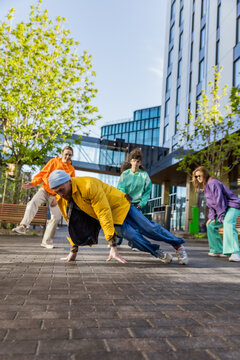Vertical Screen: Young And Athletic Caucasian B-Boy Breakdancing To Break Beats On The City Street Among Modern Buildings In The Circle Of Friends. Fashionable People Supporting Professional Dancer