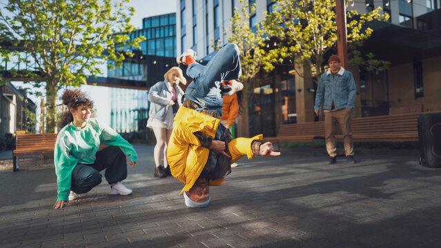 Vibrant Outdoor Scene Capturing A Diverse Group Of Young Adults Energetically Breakdancing In An Urban Setting, Showcasing Youth, Culture, And Friendship With A Modern Architectural Background.