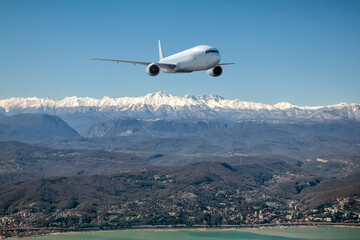 A white wide body airliner fly over resort mountain town on the seashore