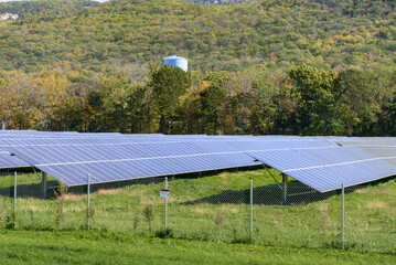 Solar power plant with rows of solar panels in a forested mountain landscape in autumn