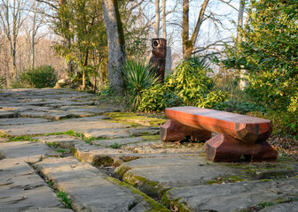 A wooden red bench on a path paved with huge stones covered with moss