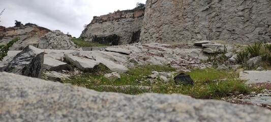 In this tranquil, immaculate landscape, one may find a green lake, rich greenery, a rocky cliff, and an overcast sky.