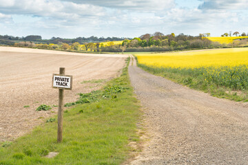 Sign post private track on farmland with trail leading into the distance flanked by fields of crops...