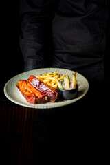 Server in dark attire presenting a plate of grilled ribs, fries, and salad, exemplifying culinary art and a delightful meal