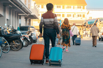 Obraz premium Back view of elderly traveler man in casual clothes dragging suitcase . Senior man walking with his luggage on street in morning. Male tourist with luggage for vacation. Vacation and travel concept.