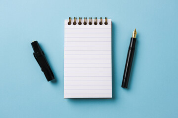 Top view of notebook and fountain pen on blue background