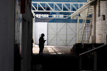 An expansive interior view of a large industrial warehouse with a silhouette of a person standing...