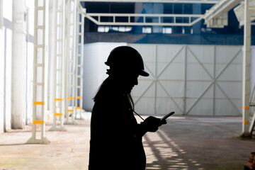 A silhouetted figure stands in a spacious industrial interior, holding a tablet, with beams of...
