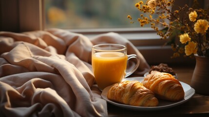 b'A warm cup of orange juice and a plate of croissants on a table near a window'