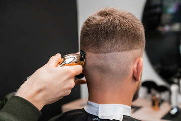Hairstylist shaves male occiput with trimmer in barbershop closeup. Professional barber cuts man hair with machine tool in hairdressing salon