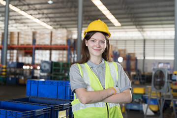 Female warehouse worker wear safety uniform, helmet standing with crossed arms in storage warehouse