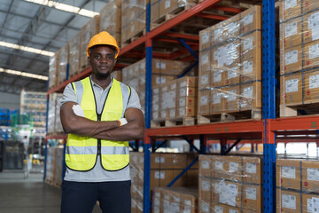 African American male warehouse worker wear safety uniform, helmet and standing with crossed arms in storage warehouse