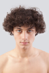 Smiling and handsome, a young man with curly hair, he looks into the camera with his blue eyes, a portrait of a guy with a bare chest isolated against a gray background