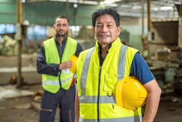 Portrait of a senior Asian industrial worker wearing safety vest and hard hat, standing in a...